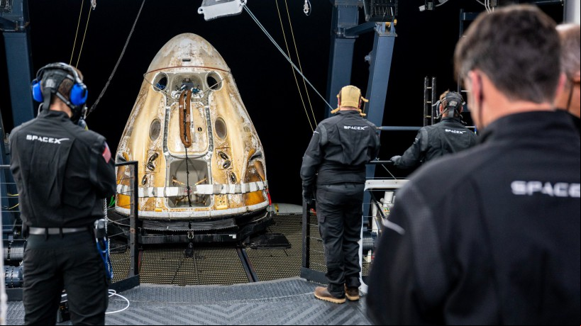 Neste folheto da NASA, as equipes de e fotográfico a bordo da nave de recuperação da SpaceX, Shannon, trabalham em torno da espaçonave SpaceX